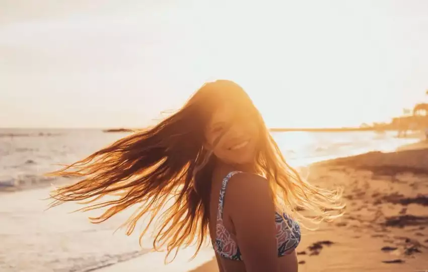 mulher sorridente na praia com cabelos tratados com vitaminas para cabelos expostos ao sol