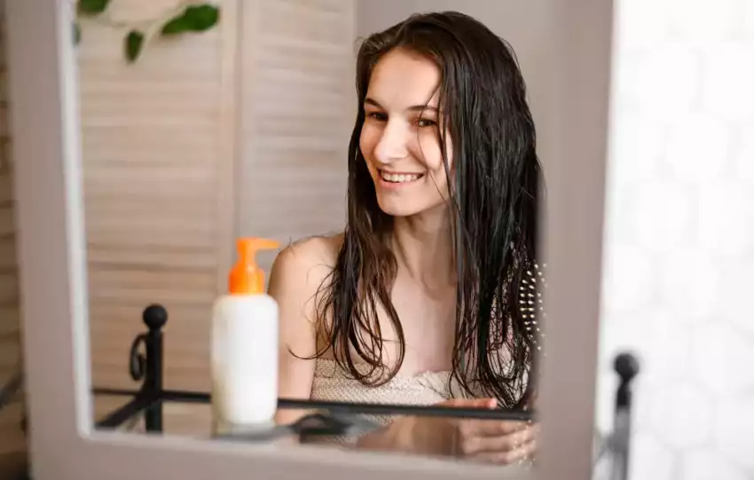 mulher-se-olhando-no-espelho-com-o-cabelo-molhado-segurando-uma-escova-de-cabelo-no-banheiro-em-frente-a-um-creme-para-hidratar-o-cabelo