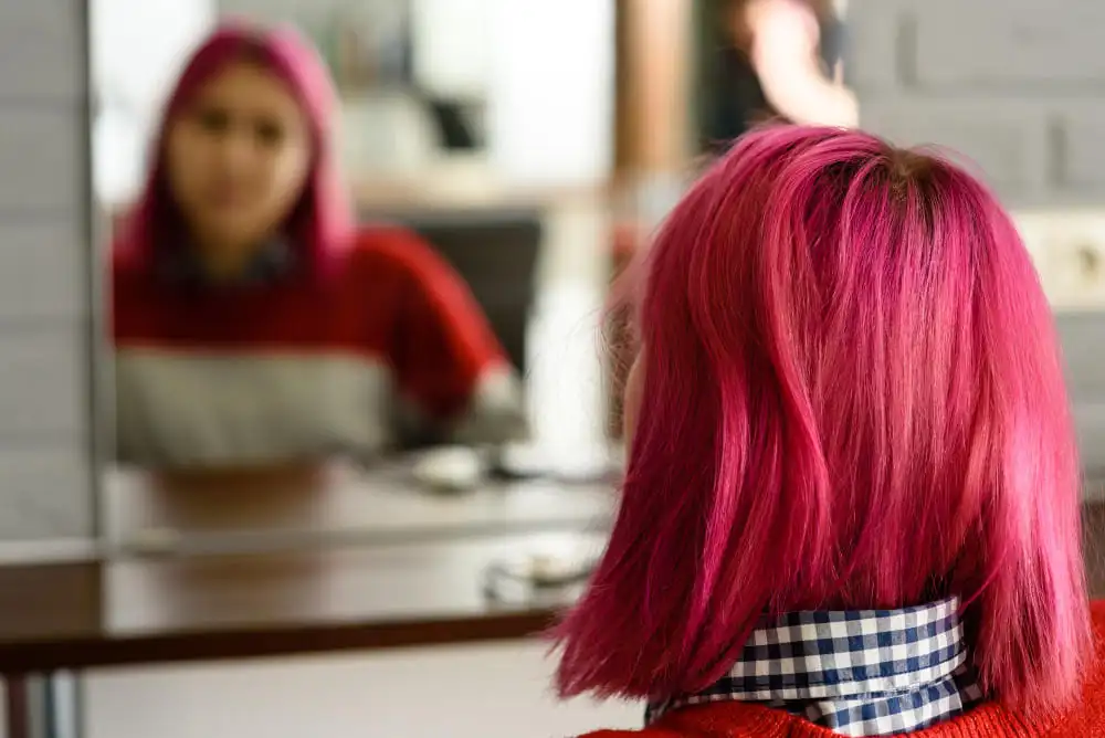 Mulher com cabelo rosa sentada se olhando no espelho
